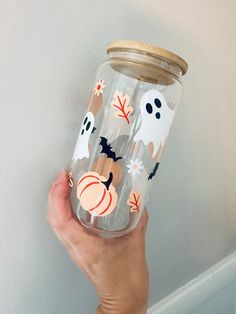 a hand holding a glass jar with halloween stickers on it and two pumpkins