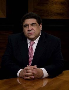 a man in a suit and tie sitting at a table with his hands folded up