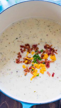 a bowl filled with soup and bacon on top of a blue table cloth next to a wooden spoon