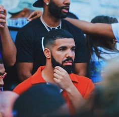 a man in an orange shirt is shaving his beard with other people around him