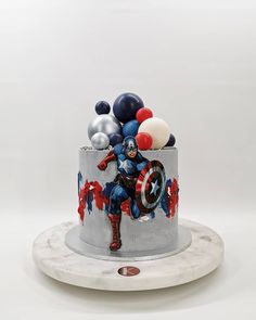 a captain america themed birthday cake with balloons on the top and an iron man figure