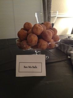 a glass bowl filled with donuts sitting on top of a table next to a sign