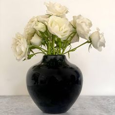 a black vase filled with white flowers on top of a gray countertop next to a wall