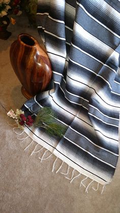 a vase sitting on the floor next to a striped blanket and some flowers in front of it