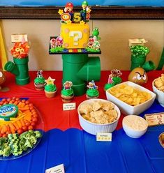 a table topped with lots of food next to cupcakes and other items on top of a blue table cloth