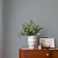 a white vase sitting on top of a wooden dresser next to a framed photo and potted plant