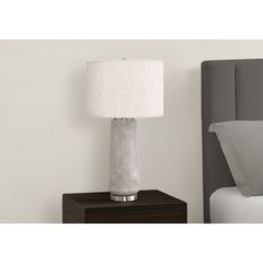 a white lamp sitting on top of a night stand next to a neatly made bed