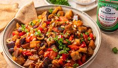 a bowl full of food next to some bread and a bottle of ketchup