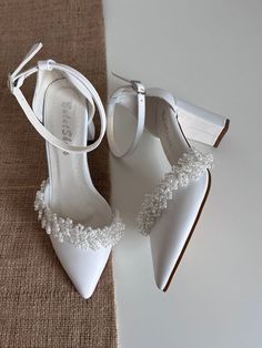 a pair of white high heeled shoes with pearls