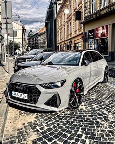 a white car parked in front of a building on a cobblestone street next to tall buildings