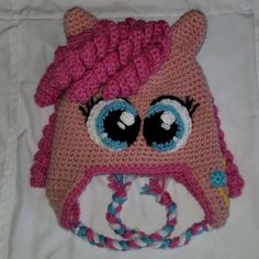 a crocheted pink hat with big eyes and a braid on the side, sitting on top of a white sheet