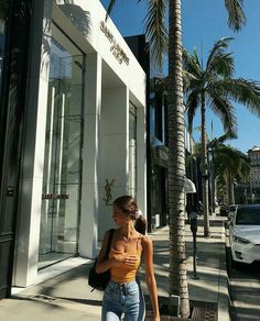 a woman is walking down the sidewalk in front of a store with her hand on her hip