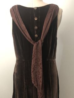 This is a stunning brown velvet dress hand created by Jane Mohr for Dress to Kill. The dress is accented with a jacquard print tie that can worn in the front or back of the dress. The dress closes with 5 flower shaped shell buttons. This dress has a fun 20's vibe. No content or size tag. Check measurements carefully, no stretch. Measurements taken with dress laying flat and doubled where appropriate. In order to determine fit we recommend comparing measurements with an item that fits you well. L Brown Maxi Dress For Formal Occasions, Formal Brown Maxi Dress, Brown Formal Maxi Dress For Fall, Brown Maxi Dress For Formal Fall Occasions, Fall Formal Brown Maxi Dress, Formal Sleeveless Brown Maxi Dress, Sleeveless Brown Maxi Dress For Formal Occasions, Brown Sleeveless Maxi Dress For Formal Occasions, Brown Long Dress For Formal Occasions