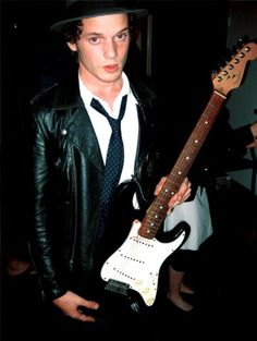 a young man in a black hat and tie holding an electric guitar with his right hand