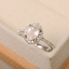 a white gold ring with an oval shaped pink stone surrounded by small round brilliant diamonds