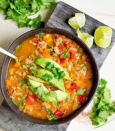 a black bowl filled with soup next to cilantro, limes and tortilla chips