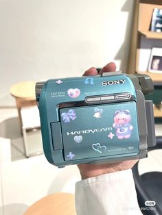 a person holding up a small camera with stickers on it's body and hands