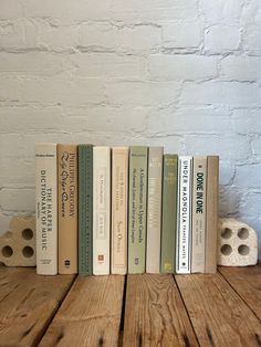 a row of books sitting on top of a wooden table next to a white brick wall