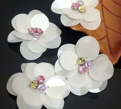 white paper flowers with pink and yellow crystals on them sitting next to an orange vase