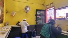 a man sitting at a counter in a restaurant next to another person with a hat on