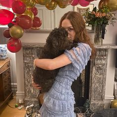 a woman in a blue dress hugging a brown dog with balloons around her and a fireplace