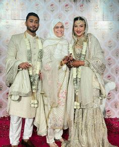 three people standing next to each other in white outfits and veils, posing for the camera