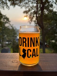 a glass filled with liquid sitting on top of a wooden table next to a tree