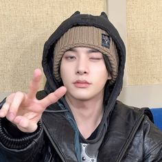 a young man wearing a jacket and hat making the peace sign