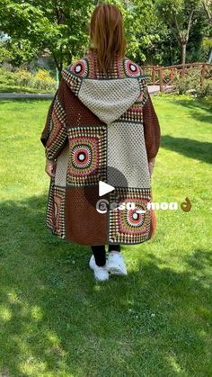 a woman standing in the grass wearing a brown and white jacket with circles on it