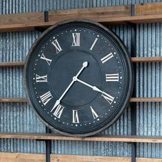 a large clock mounted to the side of a wooden shelf next to metal pipes and tubes