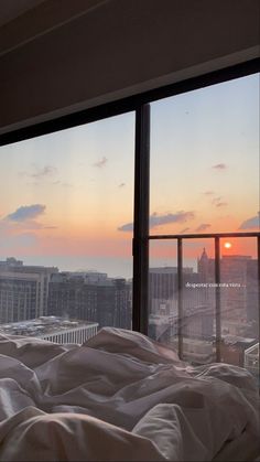 the sun is setting over a city from a bed in a room with large windows