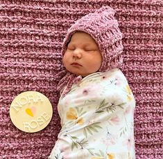 a newborn baby is sleeping next to a crocheted pink blanket with a name tag