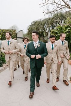 a group of men in suits and ties walking down a sidewalk with one man wearing a green tie