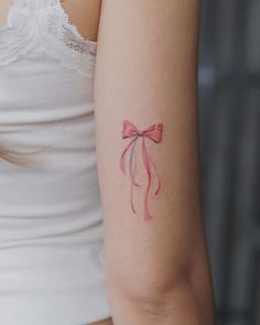 a woman's arm with a pink bow tattoo on the left side of her arm