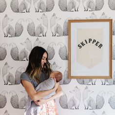 a woman holding a baby in front of a wallpaper with animals and the word skipper on it