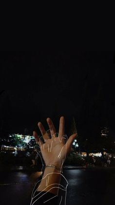 a person's hand reaching up into the air at night with lights projected on it