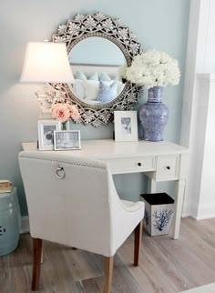 a white desk topped with a mirror and vase filled with flowers next to a lamp