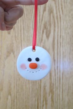 a hand holding a white ornament with a snowman face hanging from it