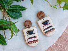 two wooden earrings with different designs on them sitting next to a potted green plant