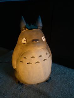 a lamp that is shaped like a totoro sitting on the floor with its eyes open