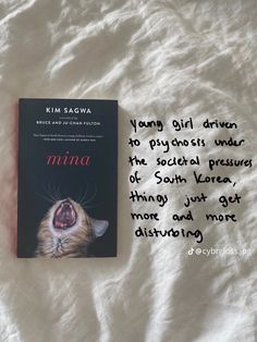 a book with an image of a cat yawning next to it on a bed