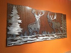 a metal wall hanging on the side of a orange wall with deer and pine trees