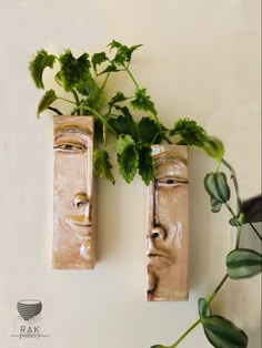 two clay faces with plants growing out of them on the wall next to each other