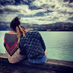 a woman sitting on top of a wooden pier next to the ocean