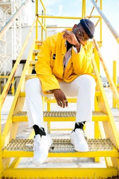 a man sitting on top of a yellow metal step ladder next to a white and black hat