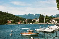 several boats are docked in the water near some buildings and mountains on either side of the lake