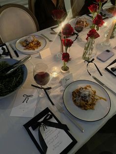 the table is set for dinner with red roses in vases