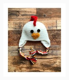 a crocheted chicken hat with a red ribbon around it's neck on a wooden floor