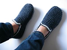 a person's feet wearing blue slippers on top of a white floor next to a pair of jeans