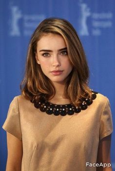 a beautiful young woman standing in front of a blue wall wearing a brown top and black beaded necklace